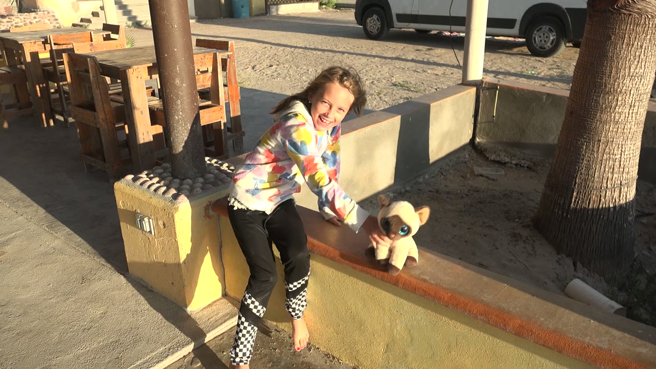Girl smiles while holding a stuffed animal near a patio wall.