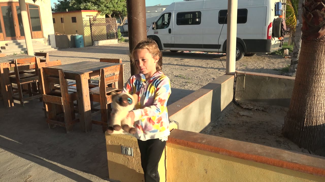 Child steps forward while holding the small animal near courtyard furniture.