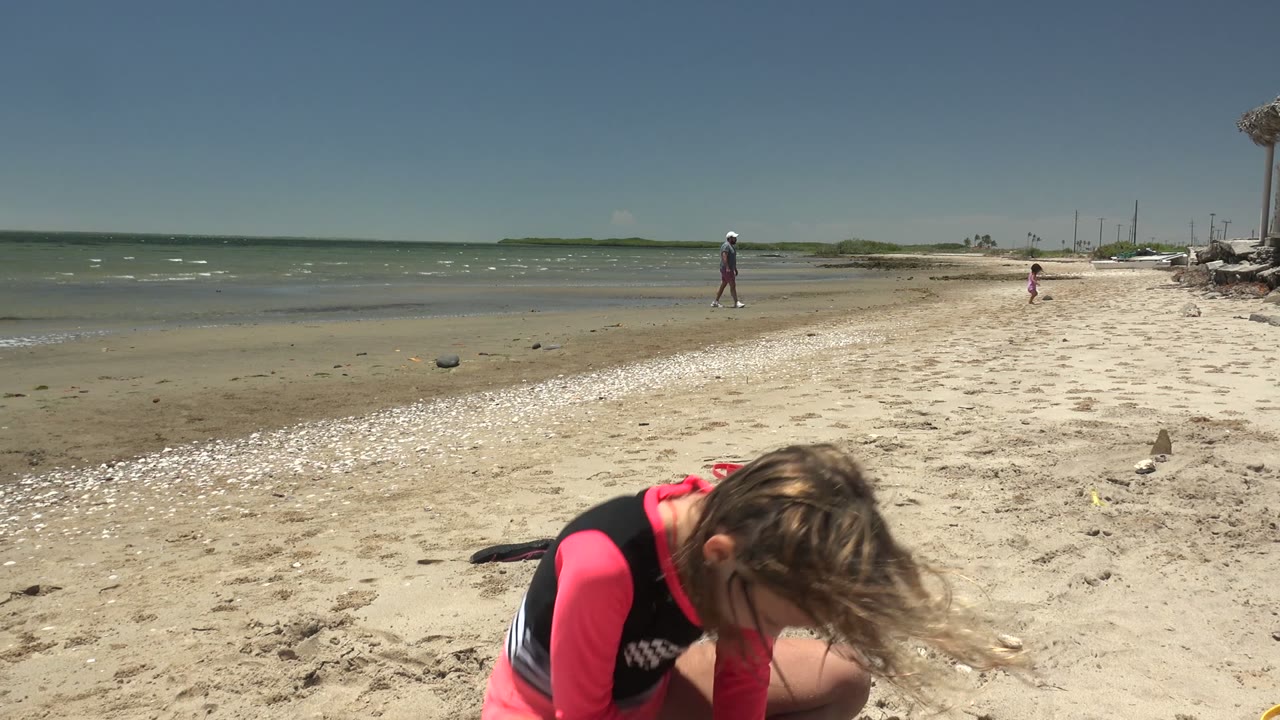 Girl crouches low in the sand near the shoreline.