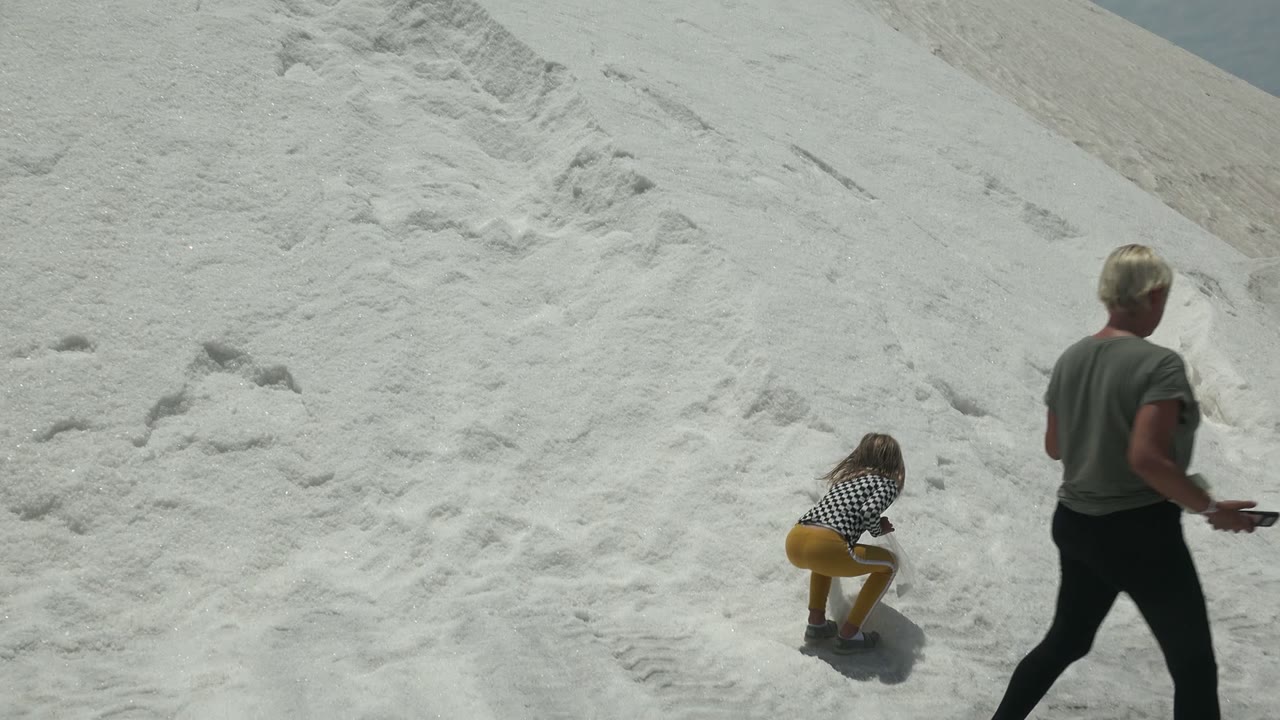 The child crouches on the white sand while the adult in a gray shirt continues walking toward the right edge of the Guerrero Negro BCS Mexico frame.