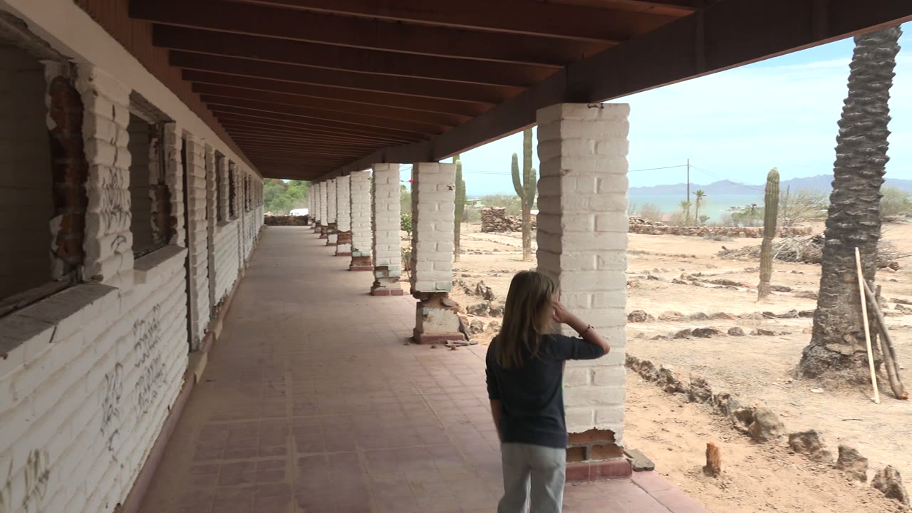 Girl near a white column on a covered walkway facing the desert.