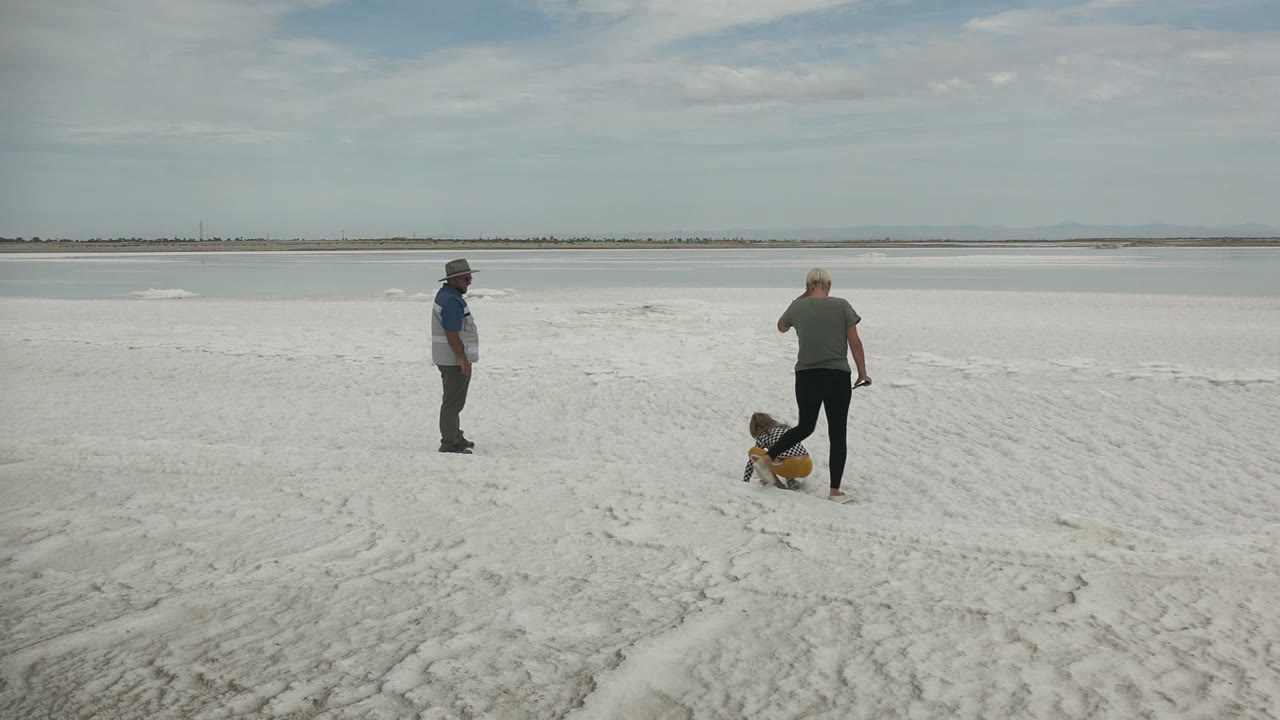 Two adults walking as a child crouches on a sandy shoreline.