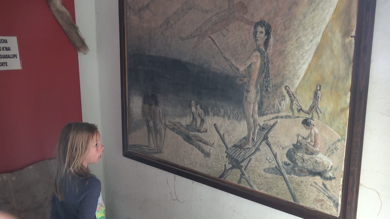 Girl looks toward a large framed painting on a red and white wall.