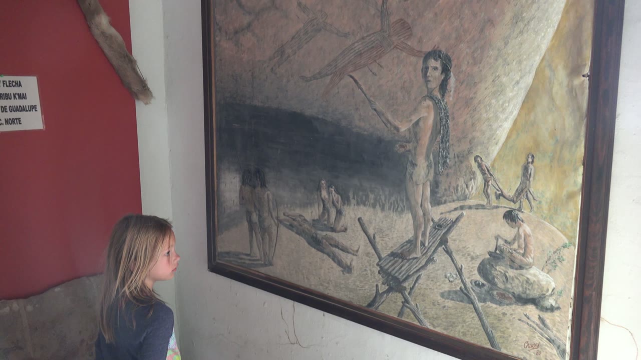 In Mulege BCS Mexico, the girl remains in profile near the lower left while the framed historical painting fills most of the wall space.