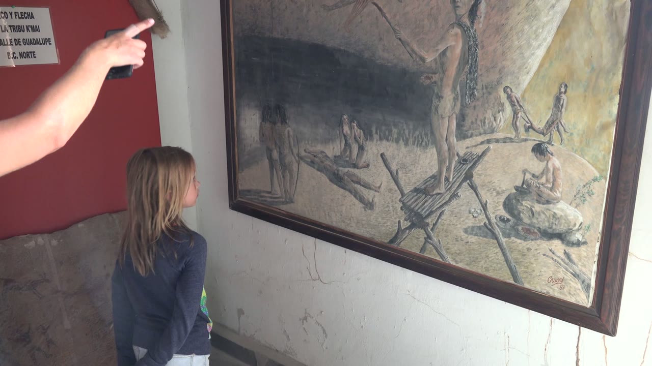 Pointing hand enters above a girl facing a framed painting.