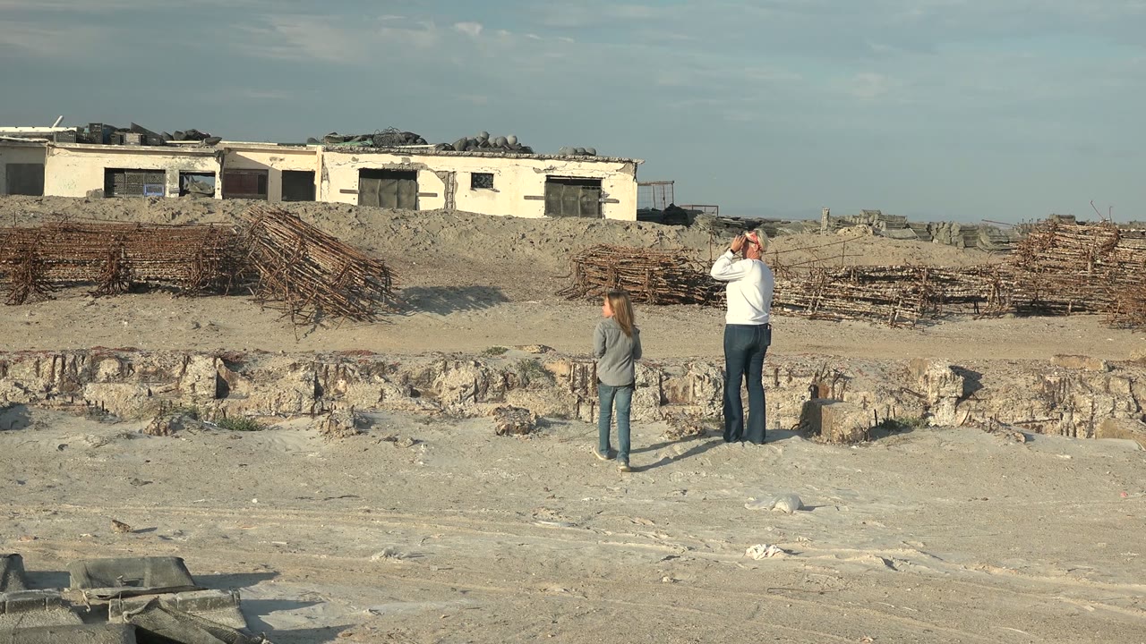 Woman closer to a man photographing at an outdoor construction site.