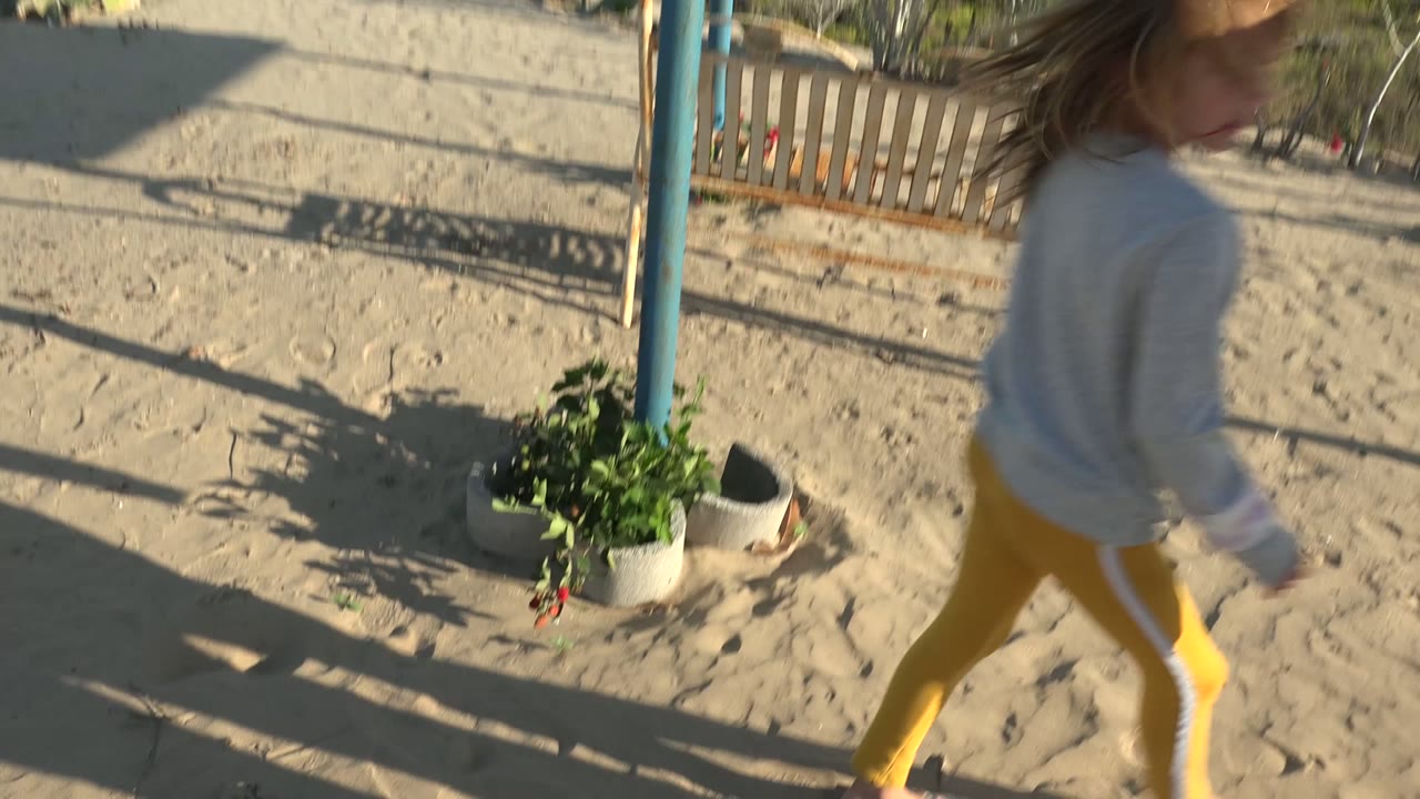 Adult and child moving past a potted plant on sand.