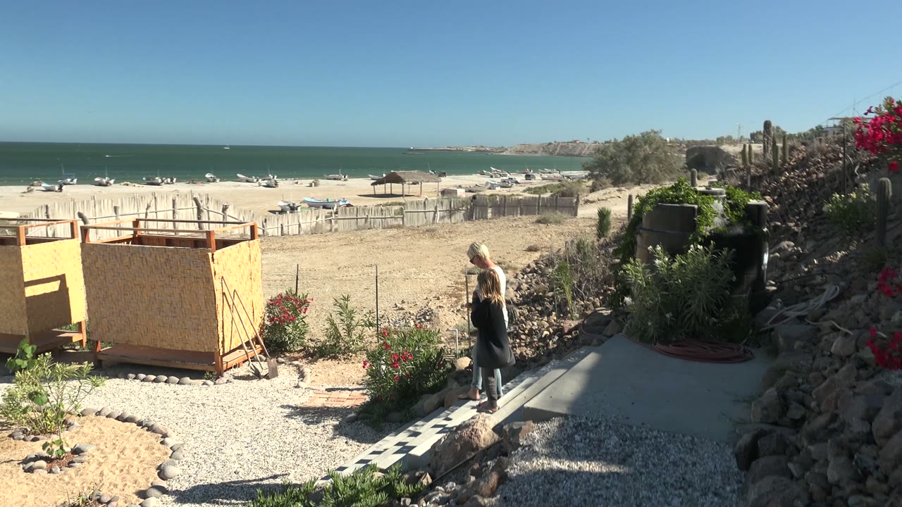 Woman continues along the gravel path near the yellow structure and beach.