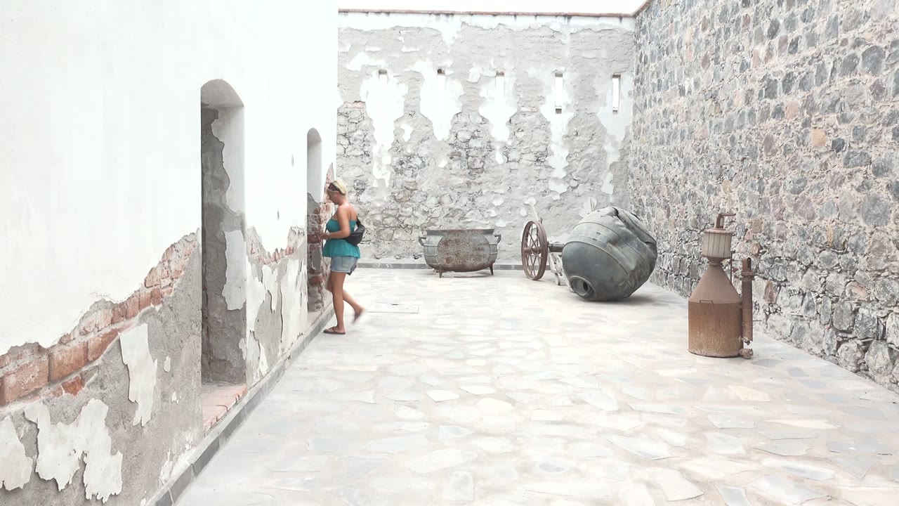 Woman near an archway in a courtyard with cannons and peeling walls.