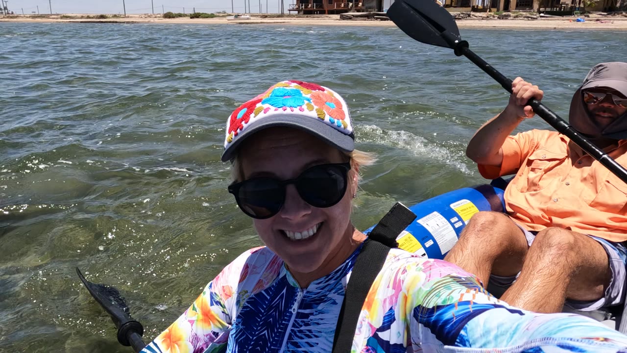 Woman smiling in a blue inflatable boat while a man paddles behind her.