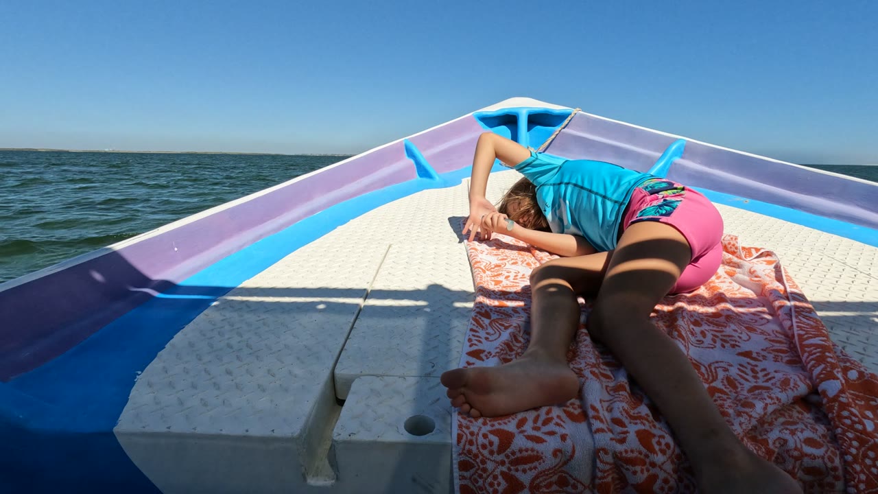 At 0:02, the person lies still on the towel as a larger angular shadow falls across the white deck in Baja California Mexico, with the ocean horizon behind the bow.
