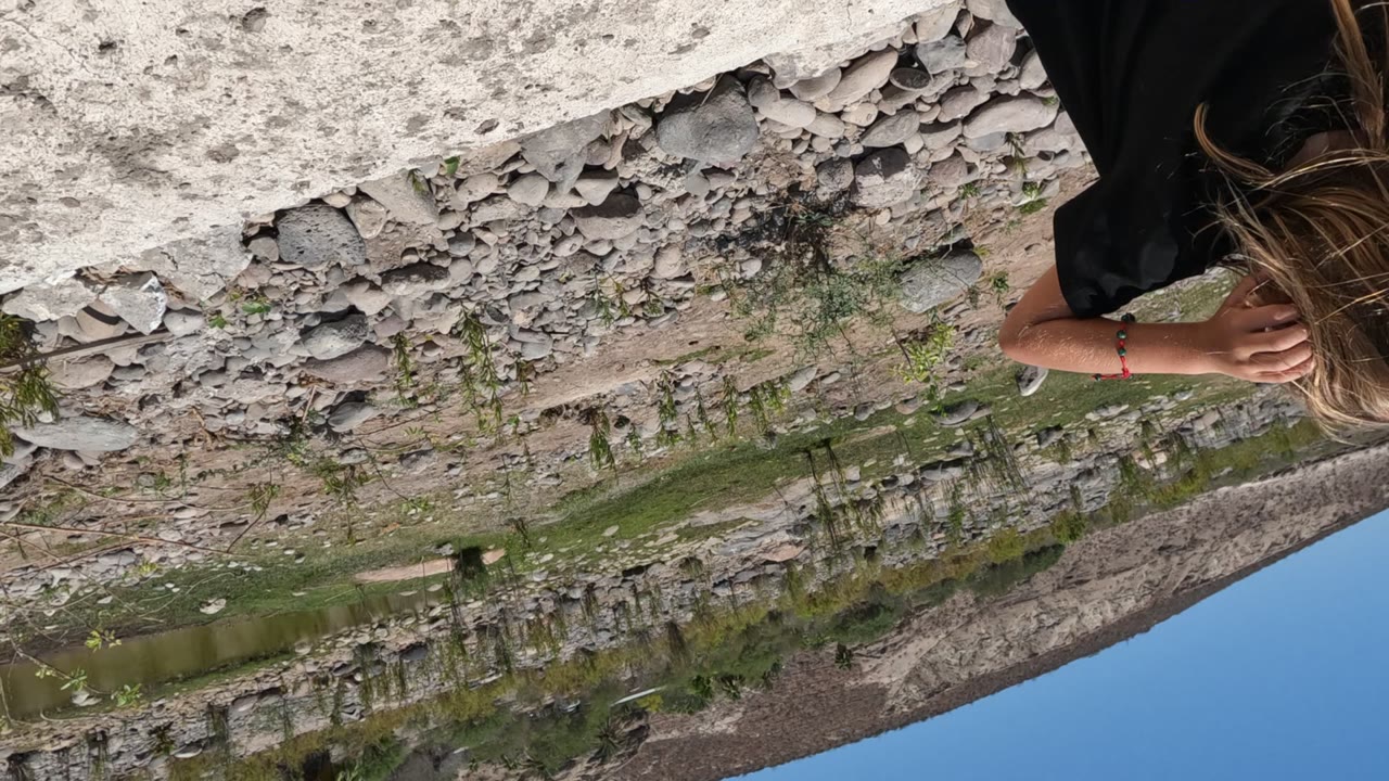 Girl with long hair walks near a peeling stone canal wall.
