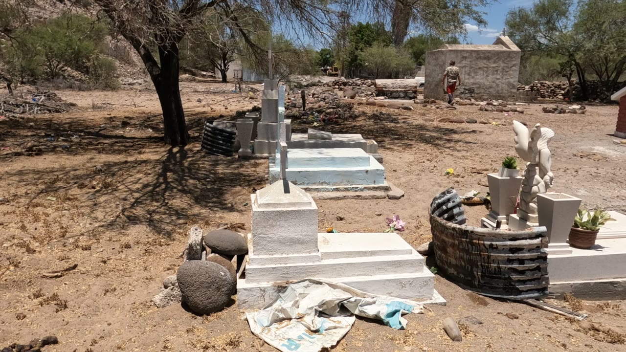 White grave markers and crosses in a dry cemetery with a person in the distance.