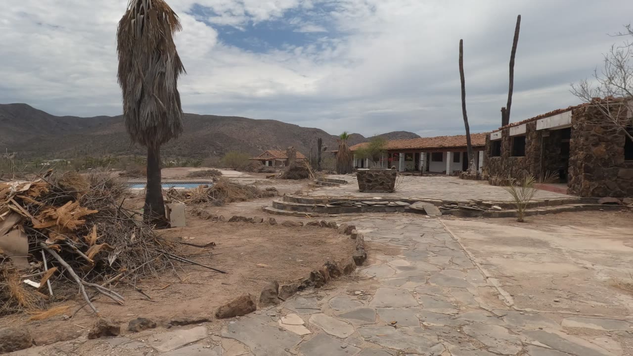 White adobe-style building beside cactus and sandy courtyard.