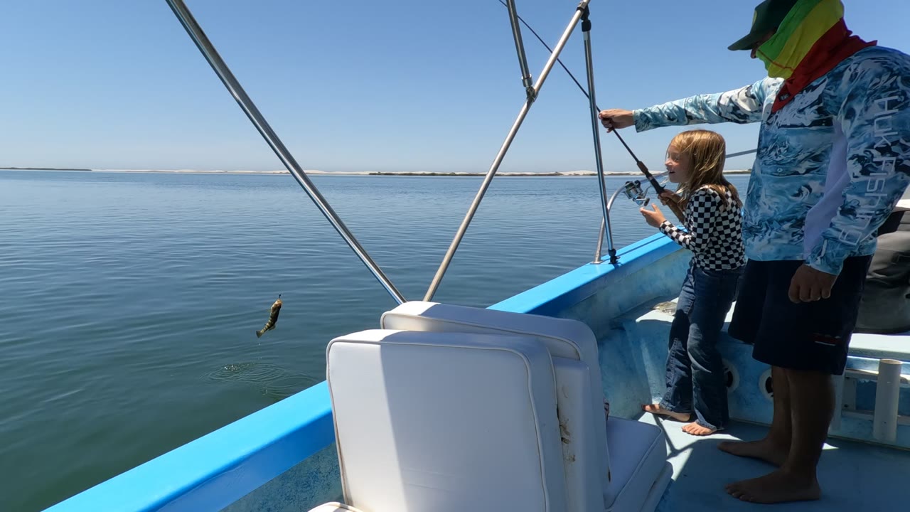 Child holds a fishing rod while an adult points over the side of the boat.