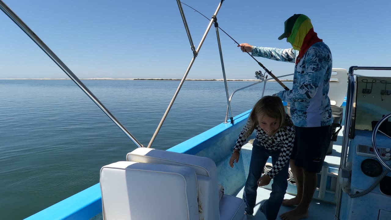 The child leans down inside the boat as the adult holds the rod near the rail, with open calm water behind them in Baja California, Mexico.