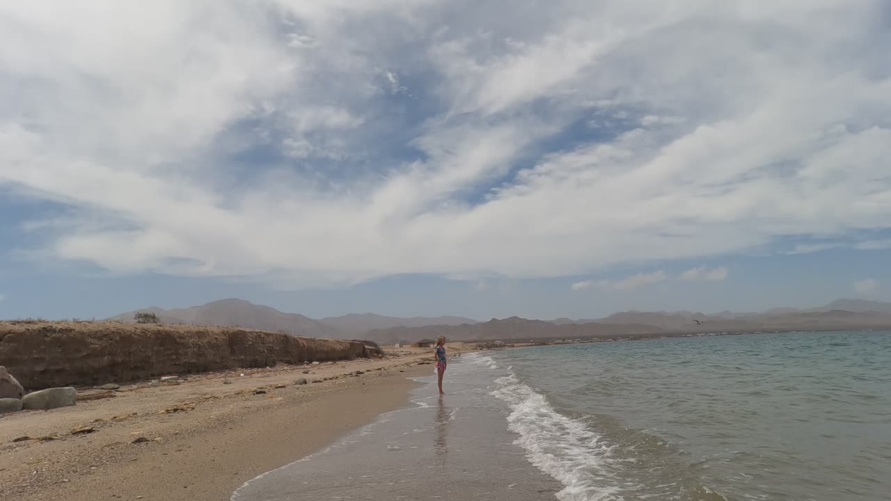 Person stands at the shoreline while a wave curls onto the sand.