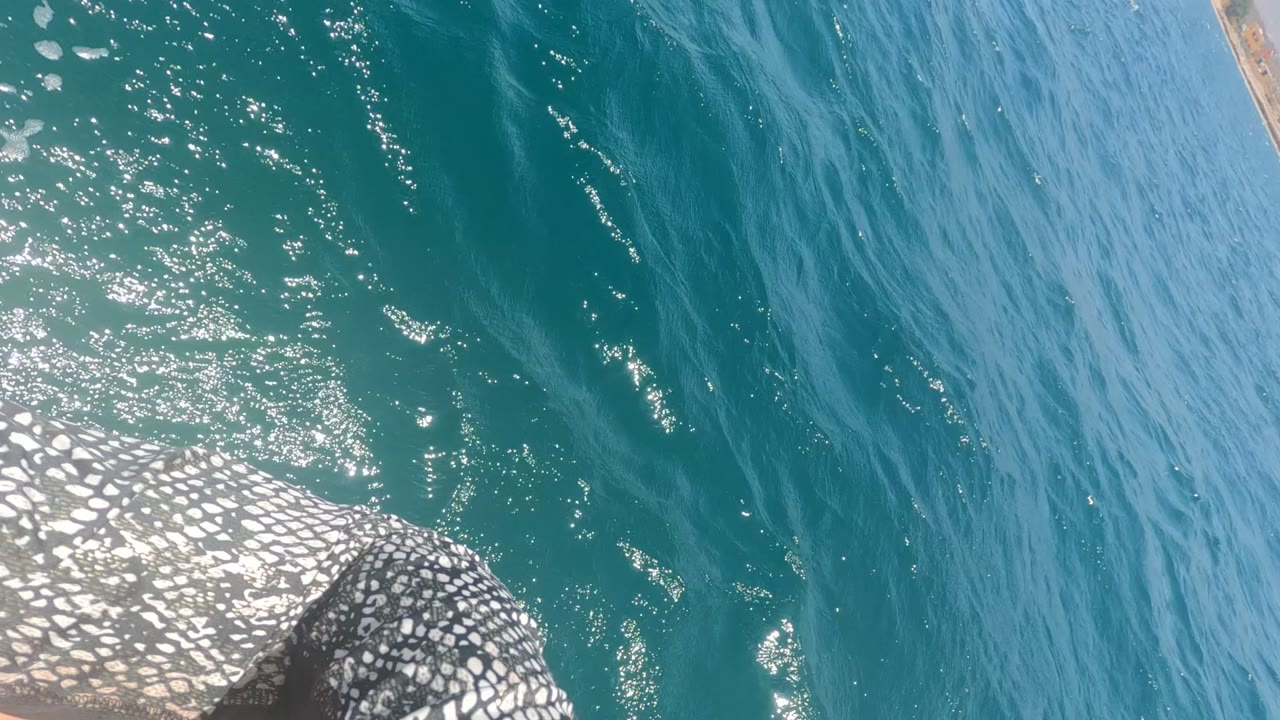 Baja California Mexico ocean surface seen from above with turquoise water, bright sun flecks, a white-and-dark patterned structure at the lower left, and no visible people.