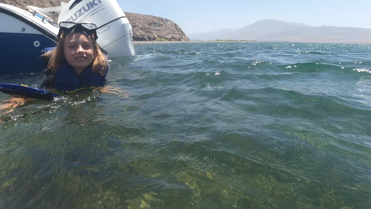Child floating in clear water beside a small boat with Suzuki outboard motors.