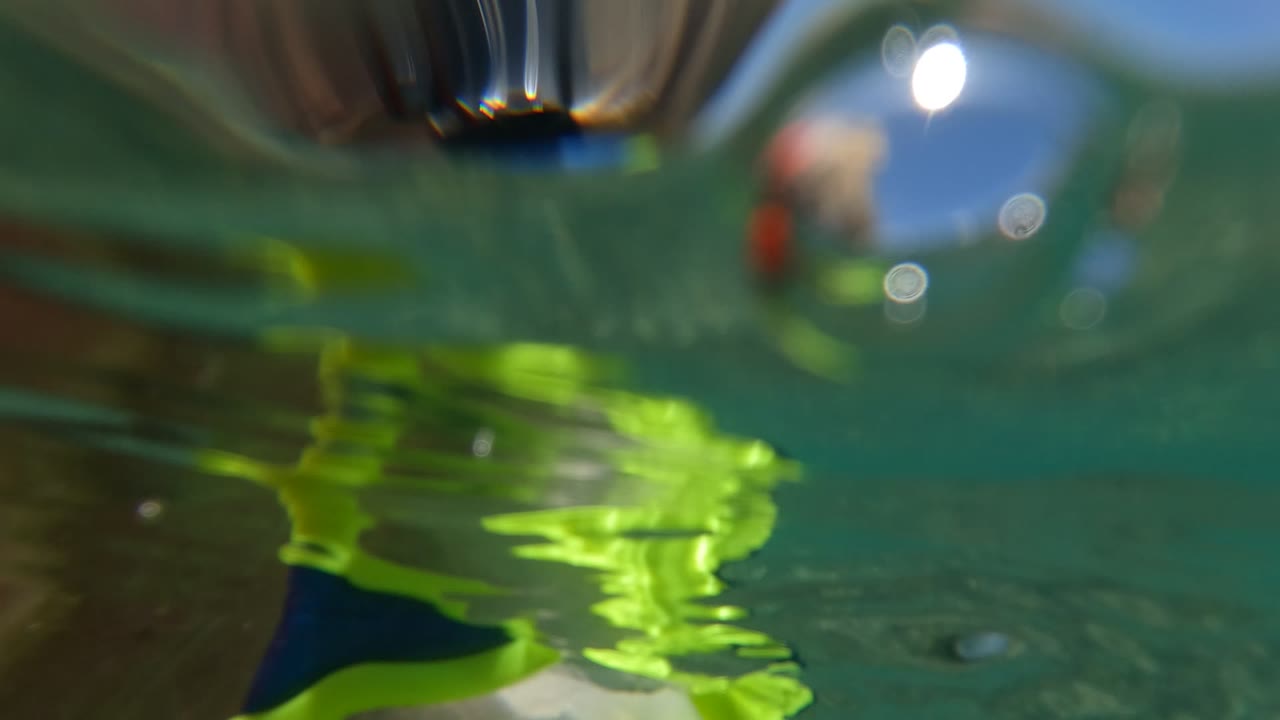 Close waterline view in Baja California Mexico with bright yellow snorkel goggles and part of a swimmer at the surface, with blurred blue sky and water reflections behind them.