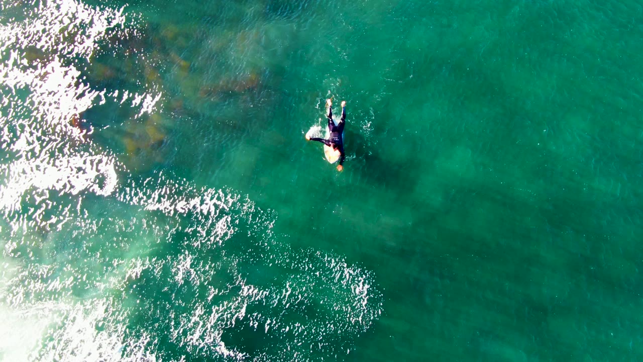 Person paddling on a surfboard beside white foam in clear ocean water.