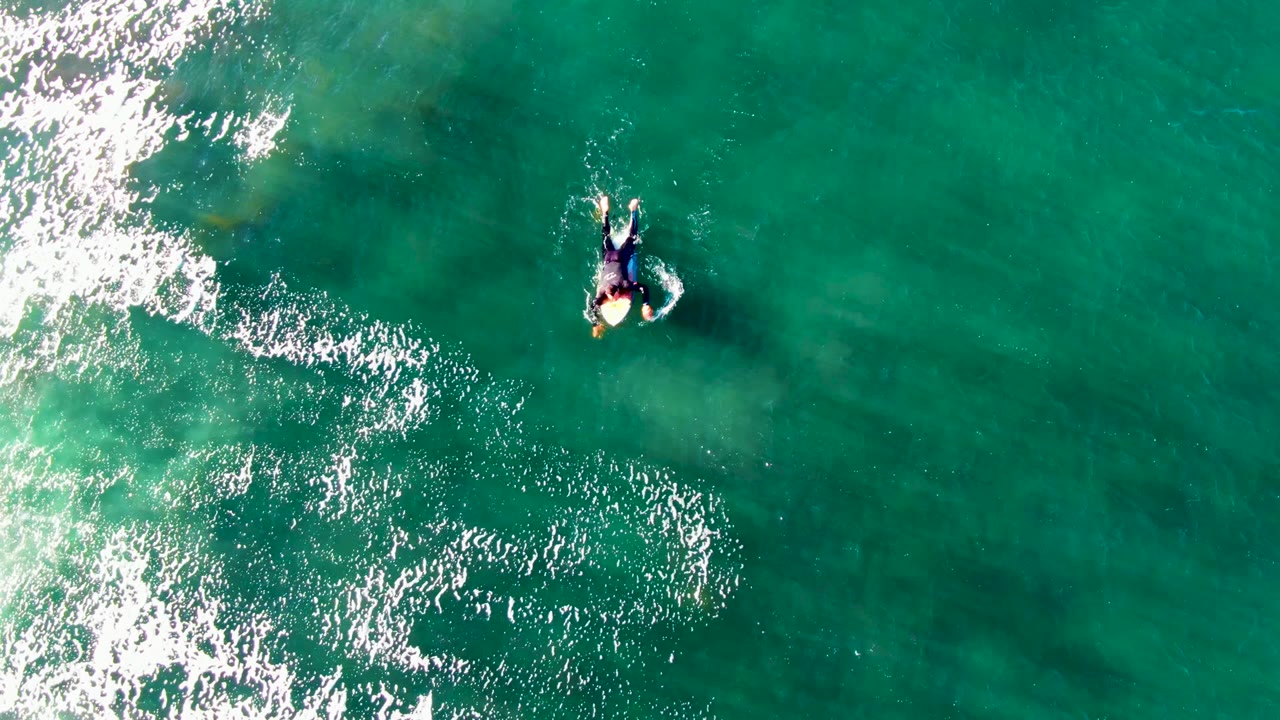 The 0:02 frame keeps the La Bocana paddler high in the composition, with a broad bright foam band on the left and darker submerged patches faintly visible under the turquoise surface.