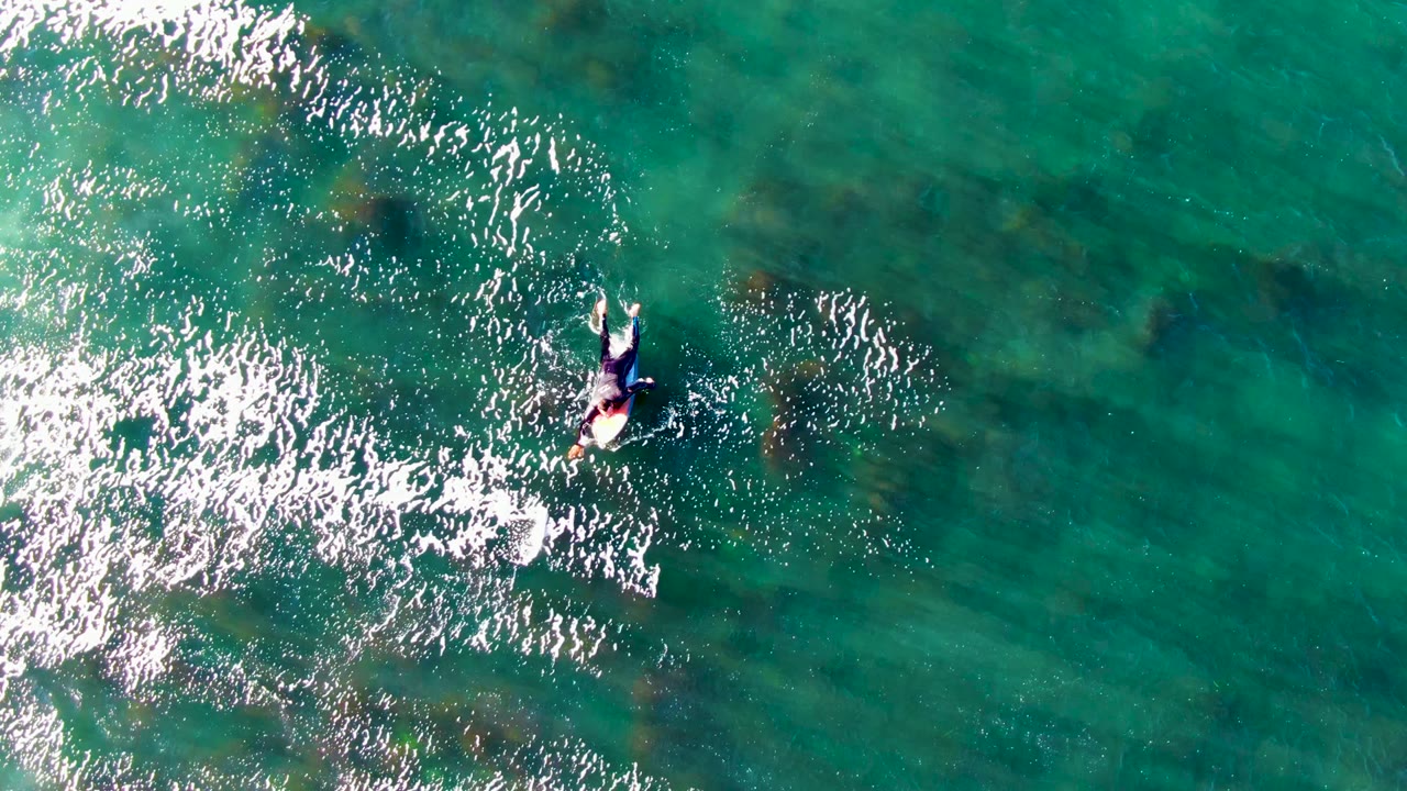 Person on a surfboard paddling beside a band of bright ocean ripples.