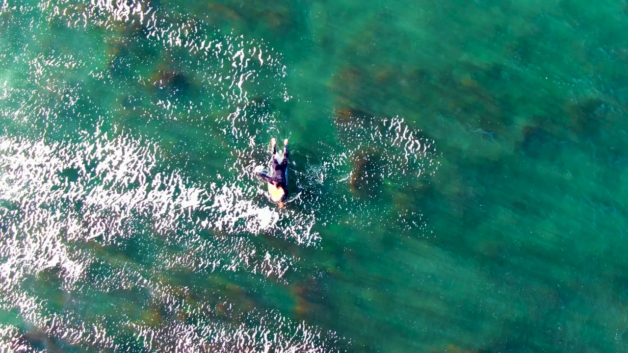 Overhead view in La Bocana with the paddler near the upper right of a broad turquoise field, surrounded by white shimmer and darker seabed areas.
