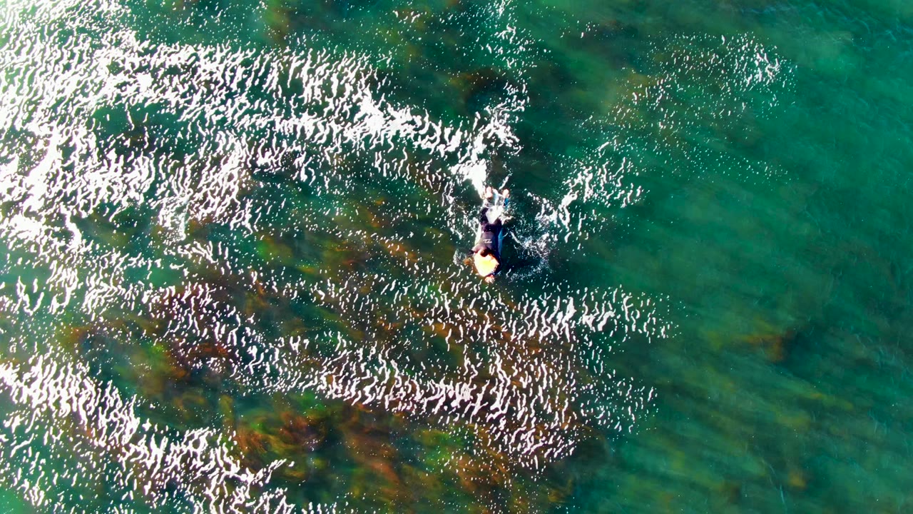 At La Bocana, Baja California Sur, Mexico, the swimmer is near the upper center as dense white reflections cross shallow green-blue water and darker vegetation patches.