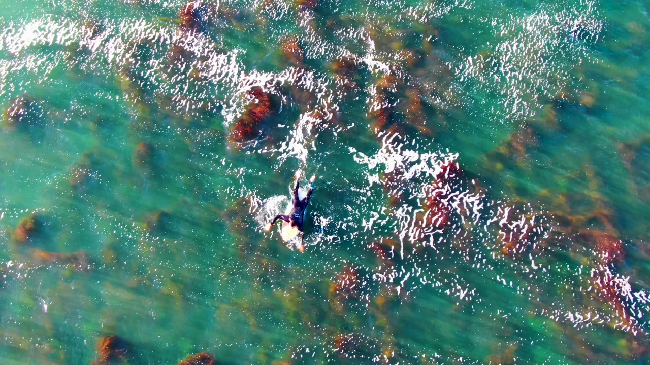 Swimmer splashing through clear turquoise water over rocky bottom.