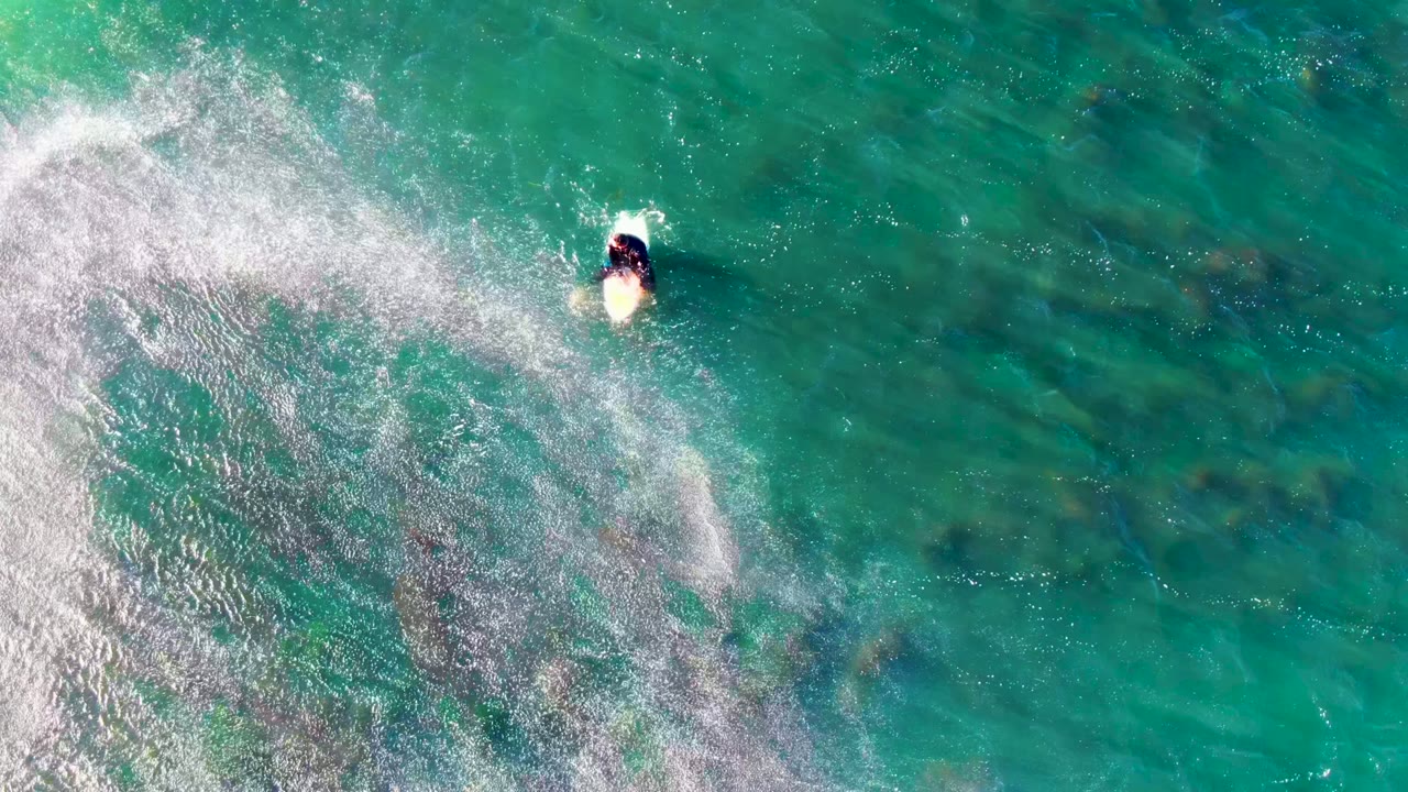 Person on a bodyboard near foamy water from above.