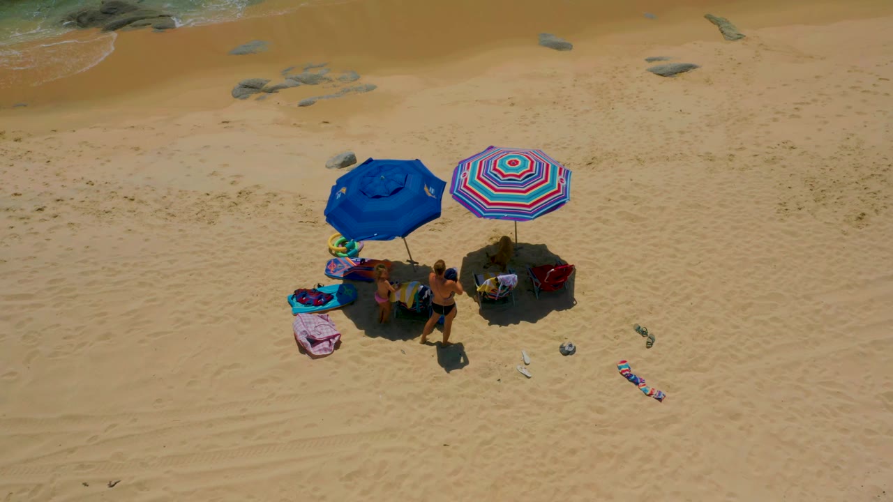 Small beach group under two umbrellas with towels and chairs spread on open sand.