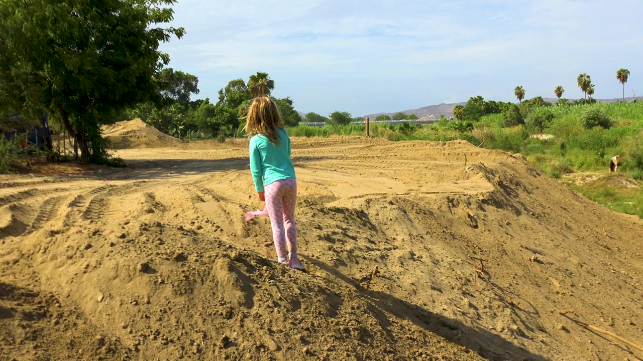 Young girl paused on a dry sandy embankment.