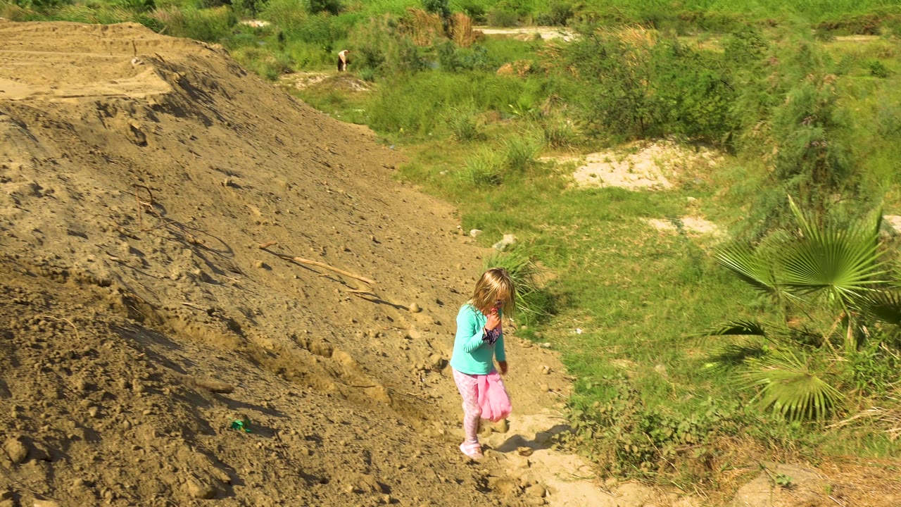 Girl walking downhill near green brush and dirt slope