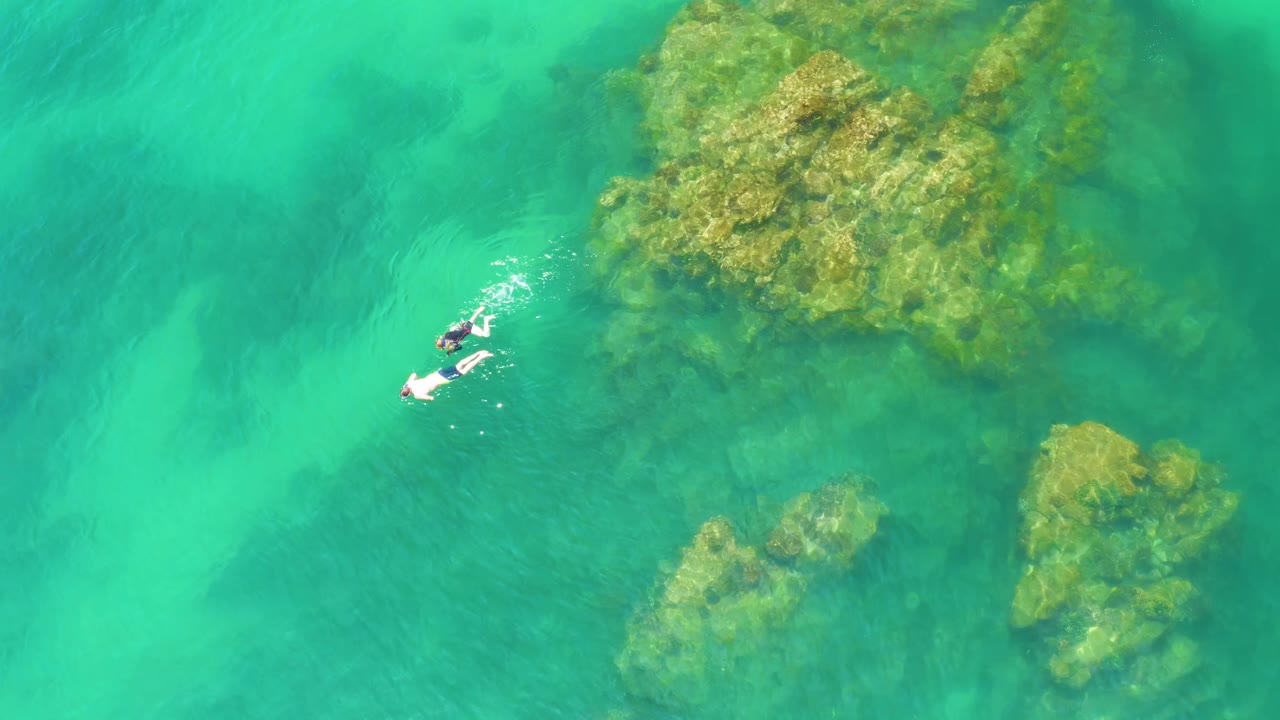 Two snorkelers creating small ripples beside underwater rocks.