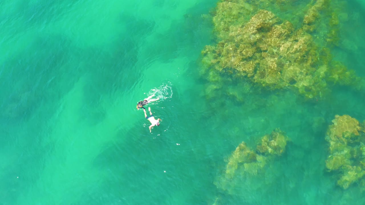 Snorkelers swimming over clear water near a rocky patch.
