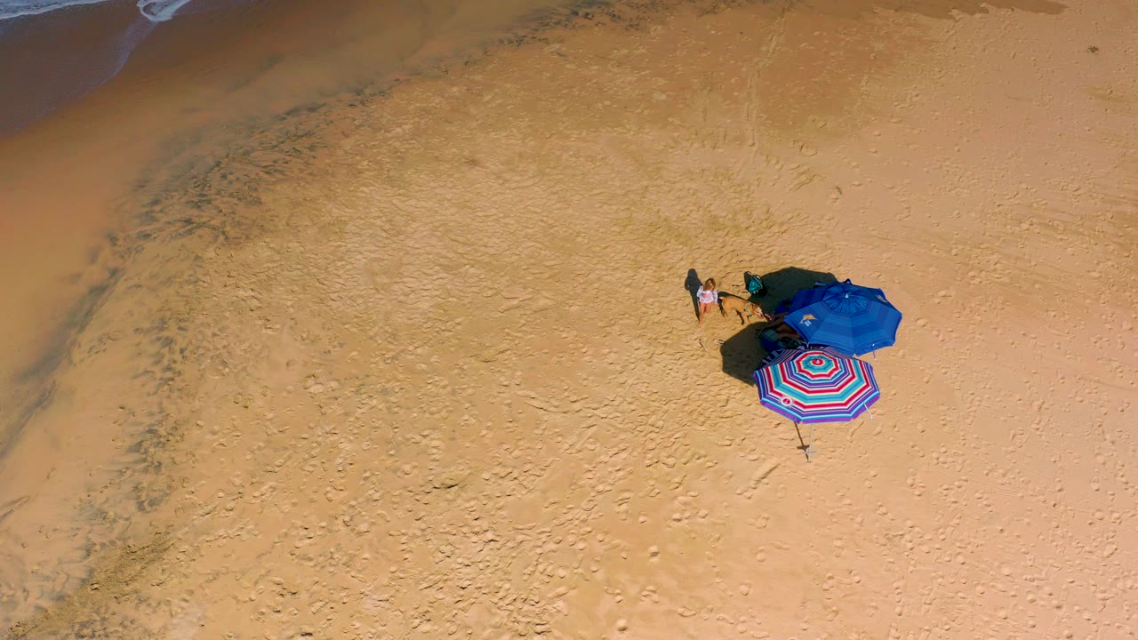 Overhead beach setup with blue umbrella and striped item on sand.
