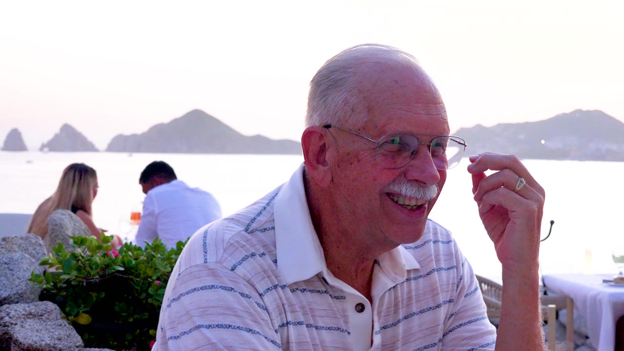 Senior man gesturing beside a seaside restaurant table