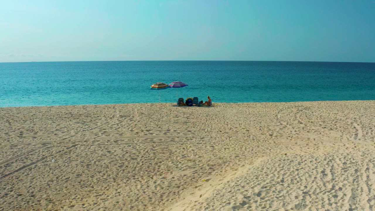 High-angle view of sandy beach, ocean horizon, umbrellas, and seated beachgoers.