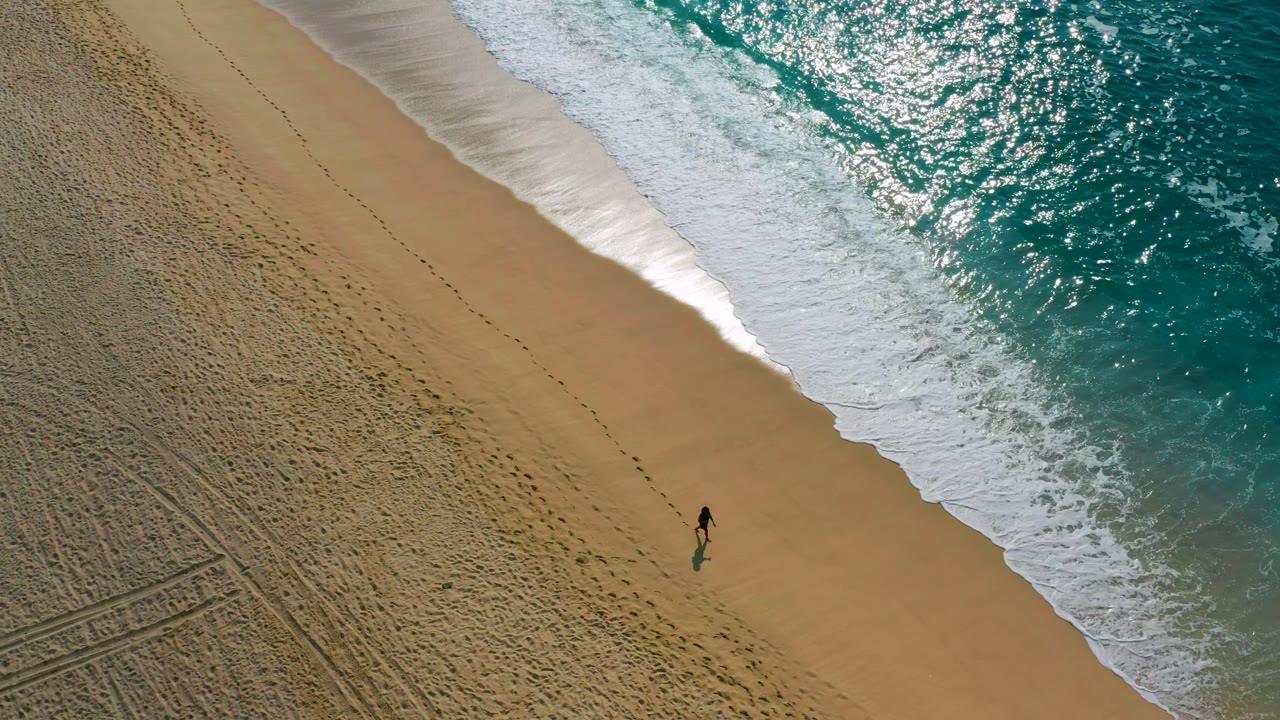 In Desert Park Natural Reserve, Baja California Sur, the person appears near the lower center of the beach as a thicker band of white surf reaches the shoreline.
