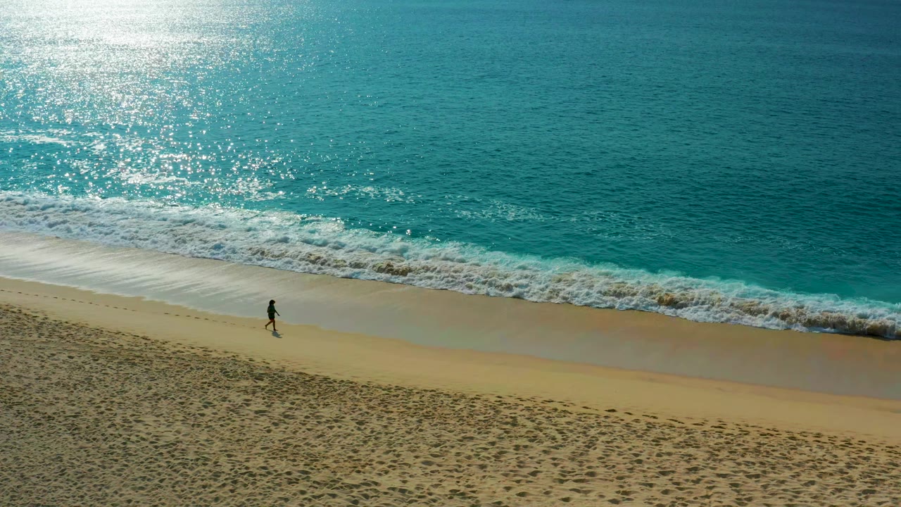 One person walks along the wet sand as waves break nearby.