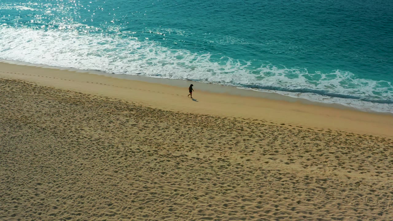 High-angle view in Desert Park Natural Reserve, Baja California Sur, with one person near the water's edge and a fresh line of surf curling across the top of the beach.