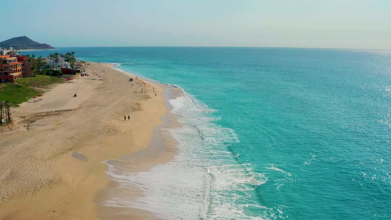 Aerial beach view with ocean on the right and low buildings on the left.