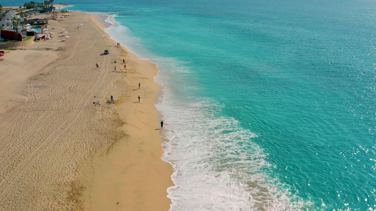 Drone view down a sandy shoreline with people near the surf.