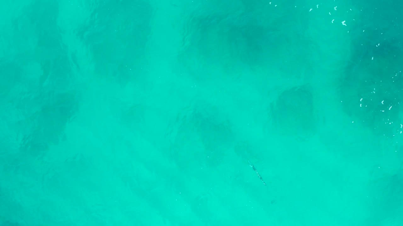 Top-down aerial view of turquoise water in Baja California Sur, Mexico, with darker submerged patches near the upper frame and no visible people.
