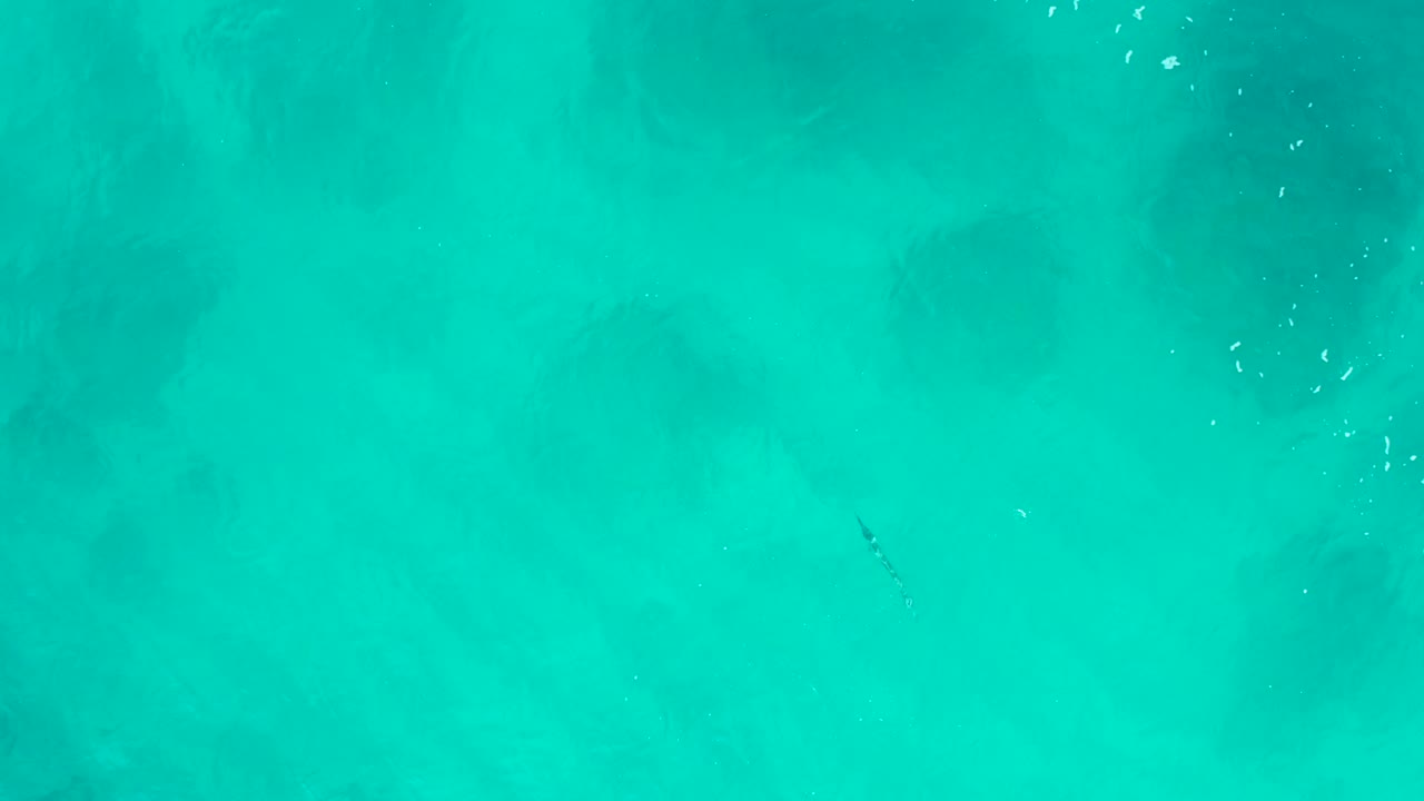 Bright turquoise water fills the frame at Desert Park Natural Reserve, with faint ripples, soft dark areas below the surface, scattered bubble flecks, and no visible people.