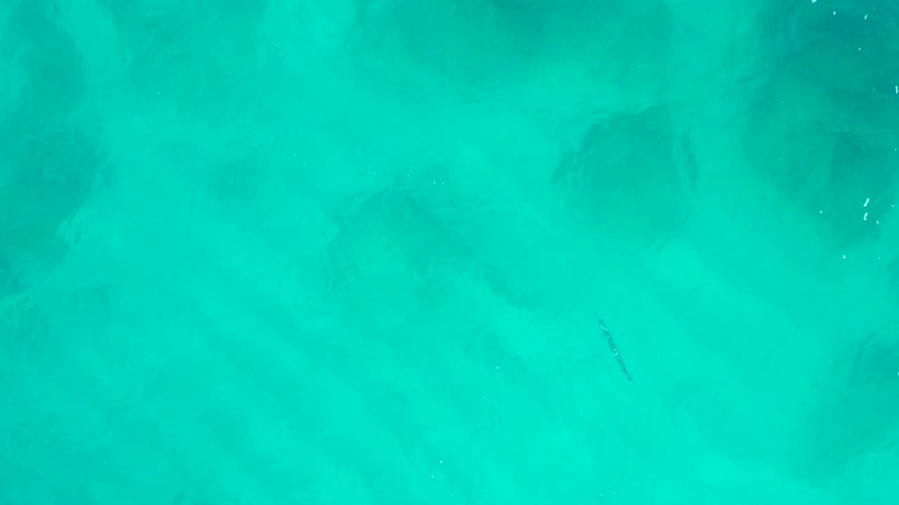 Top-down aerial frame over turquoise water at Desert Park Natural Reserve in Baja California Sur, with faint submerged dark patches and no visible people.