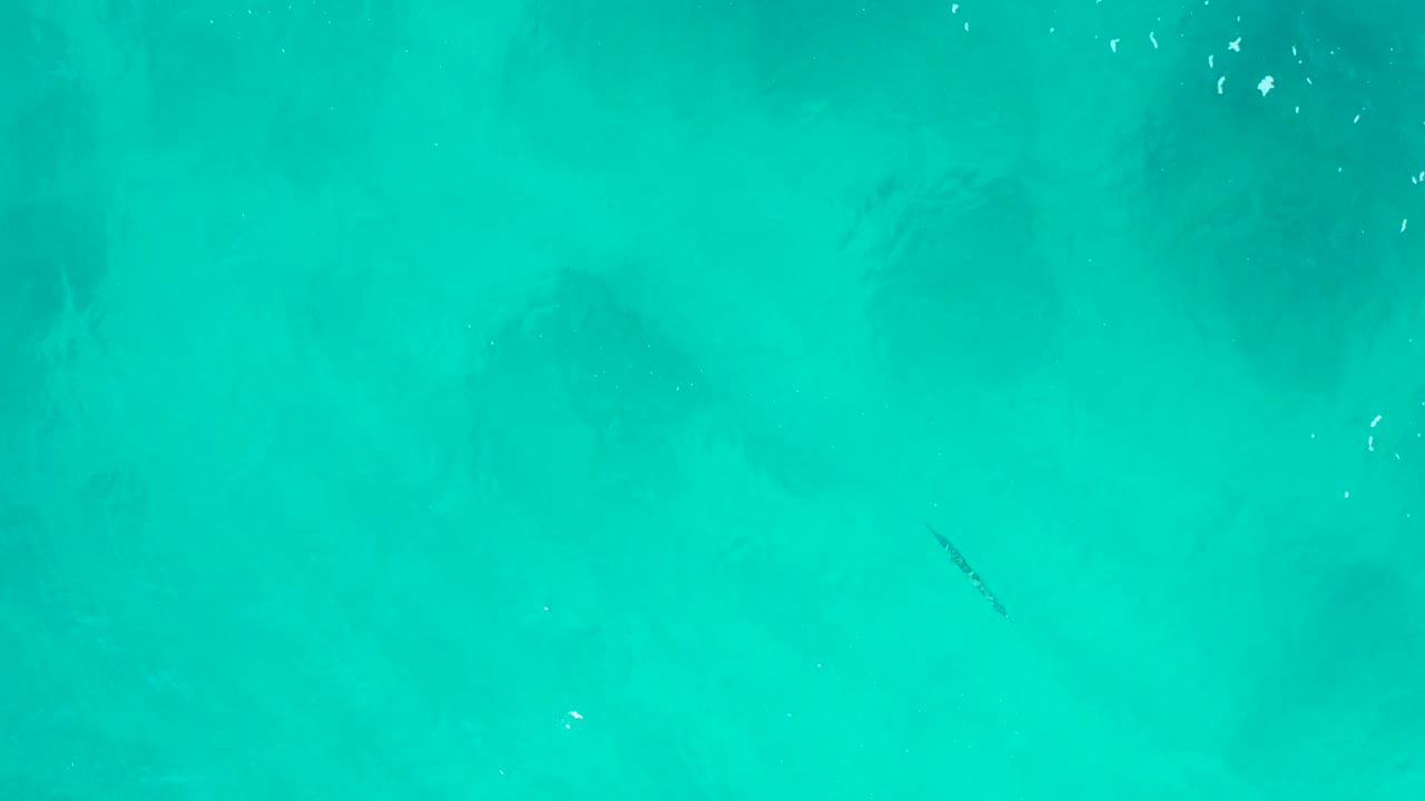 Aerial view over turquoise water at Desert Park Natural Reserve, showing soft darker underwater areas and scattered white flecks with no visible people.