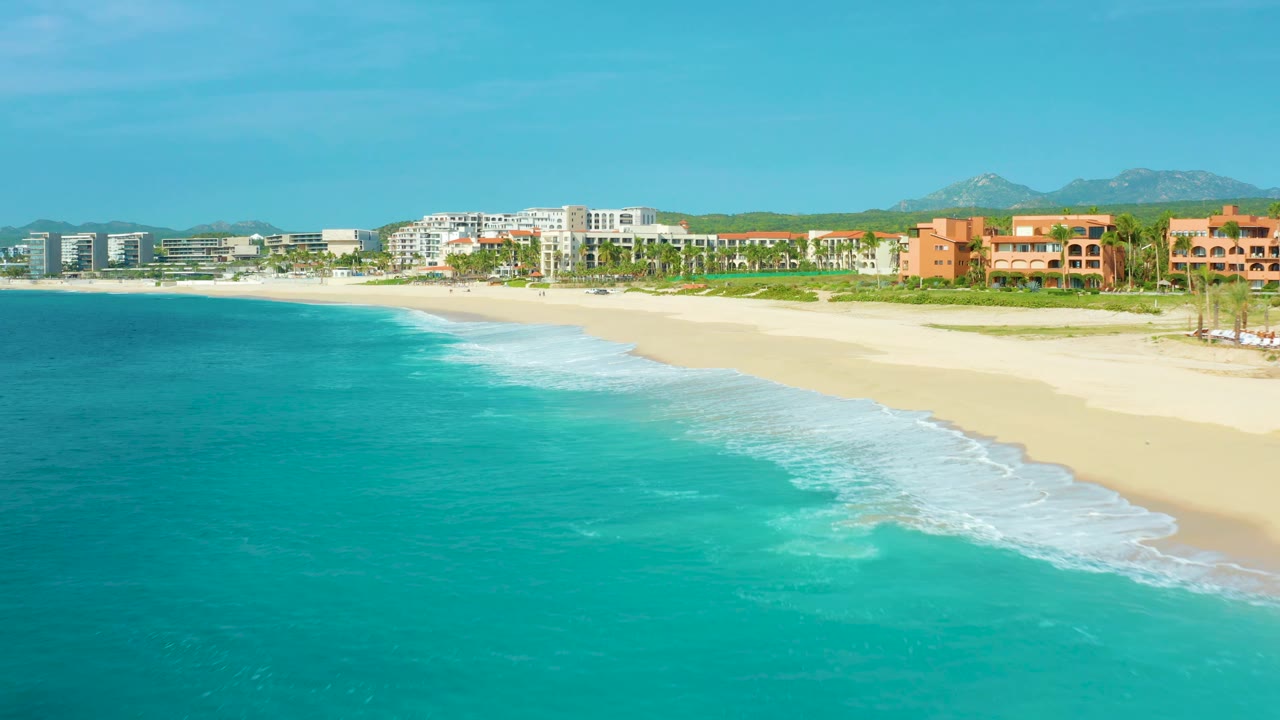 At 0:02 the aerial frame over Desert Park Natural Reserve in Baja California Sur, Mexico shows more open turquoise water, a diagonal surf line, empty pale sand, resort buildings, and no visible people.