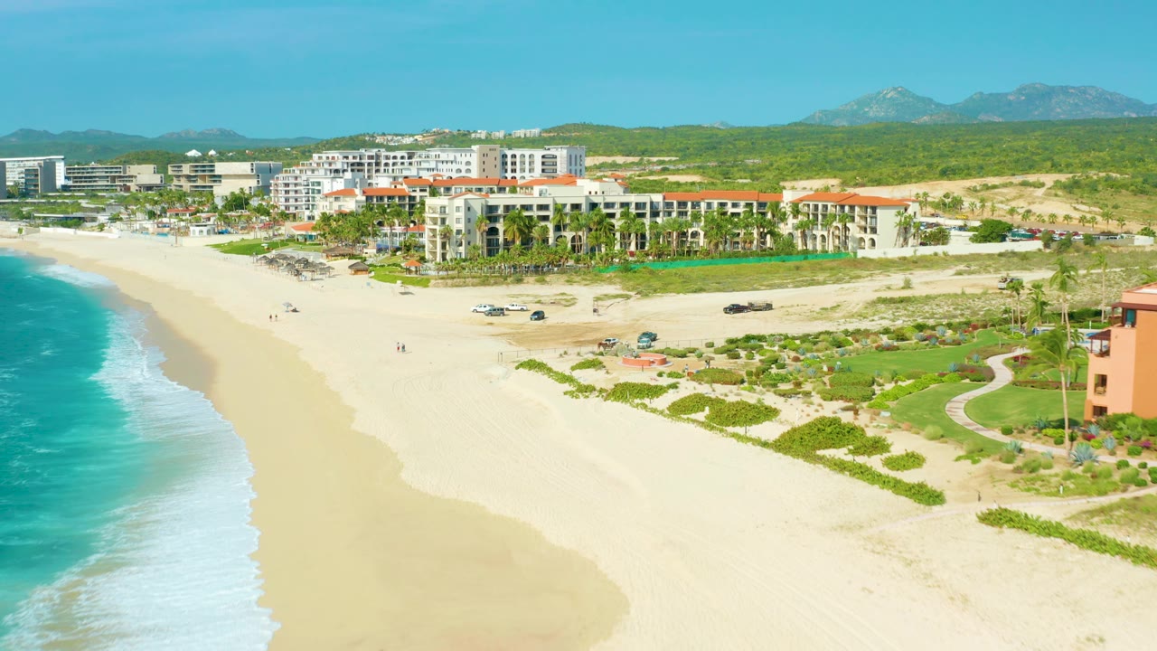 Aerial coastline view with resort buildings, beach access roads, dunes, and surf.